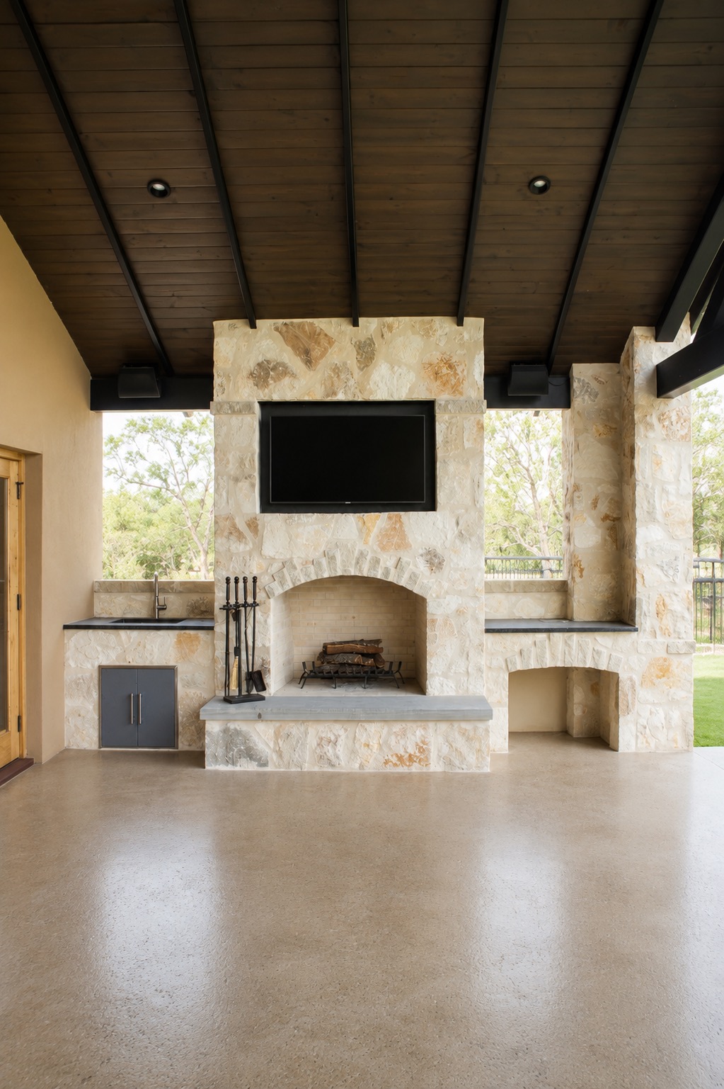 Covered outdoor living area with stone fireplace and outdoor kitchen, built by Kreifels Construction